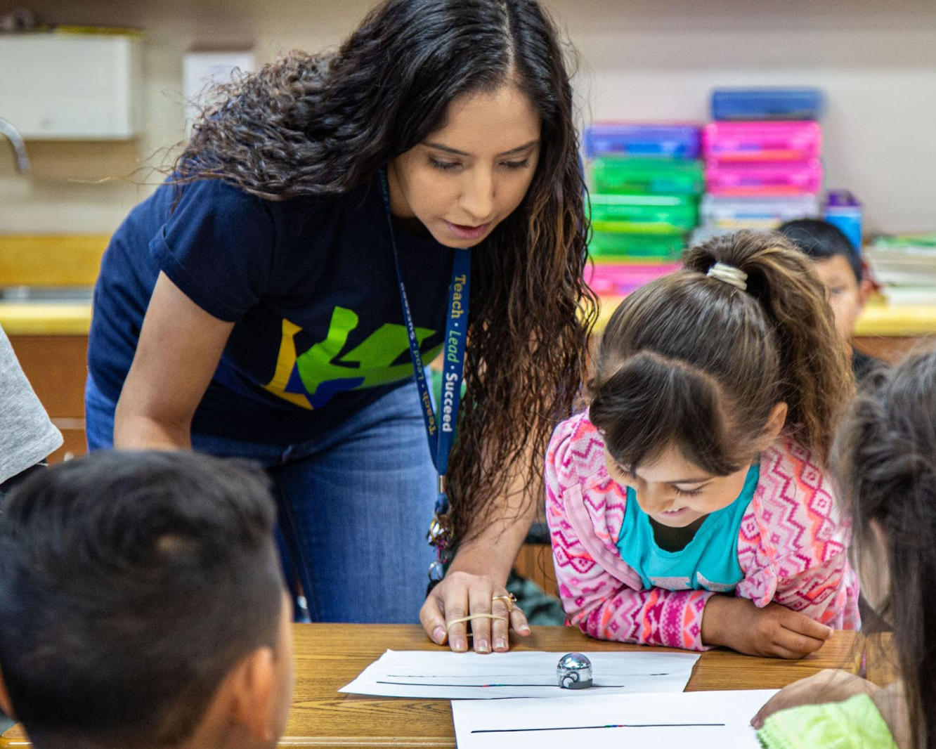 Teaching Fellow Tutor helping elementary student sitting at a desk with other students around.