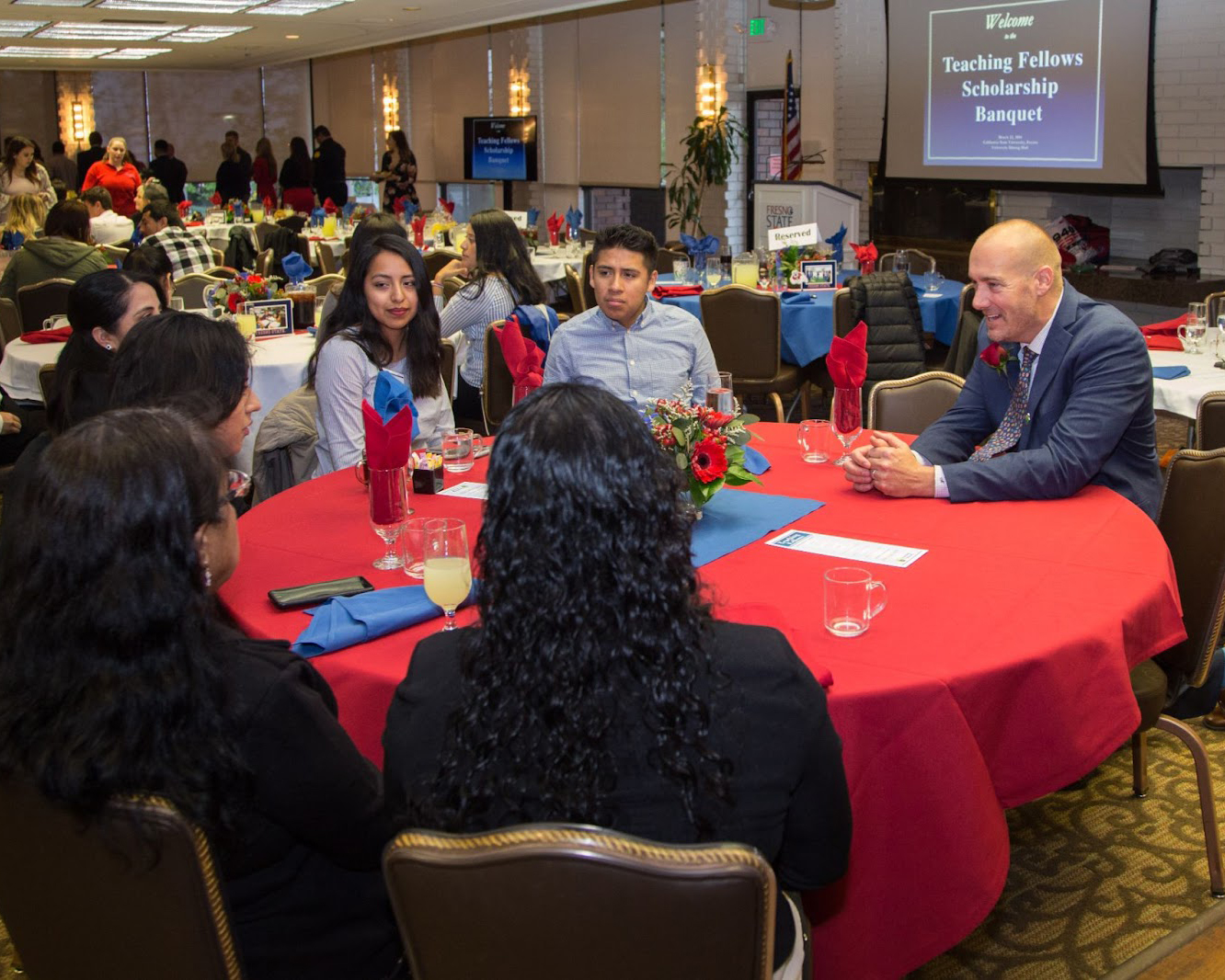 Group of six college scholarship recipients sitting at a table with a man in a suit.